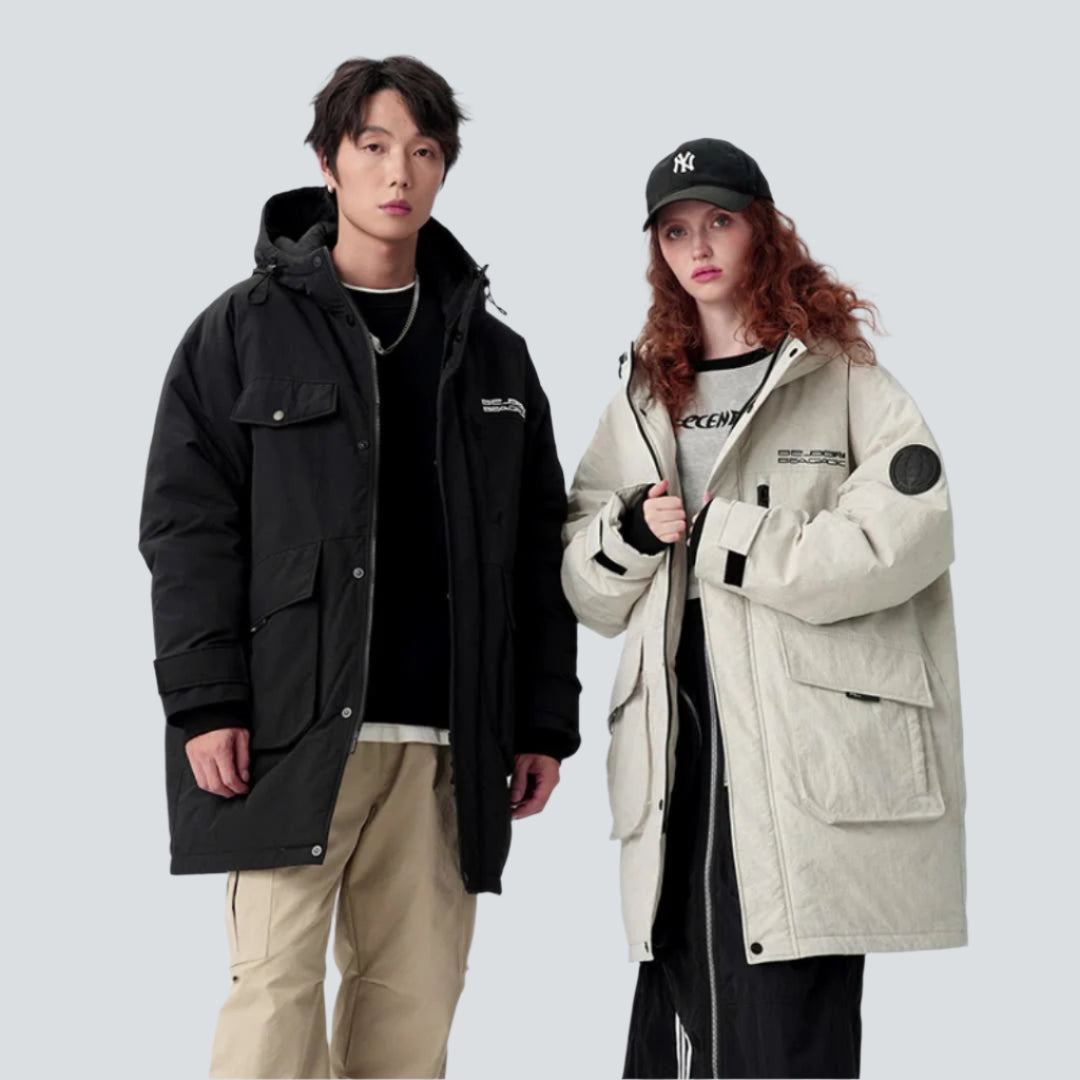 A man and woman wearing contrasting parkas stand against white background - his in black, hers in cream with NY cap