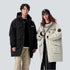A man and woman wearing contrasting parkas stand against white background - his in black, hers in cream with NY cap