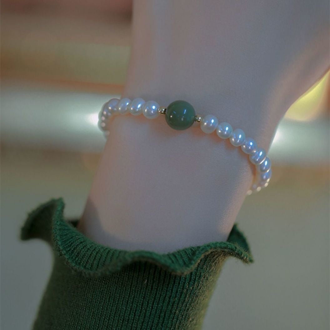 Pearl bracelet with jade green accent bead worn over green knit fabric, close-up shot showing delicate design and clasp