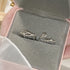 A person holding a gray velvet jewelry box displaying silver twig and rose rings nested in the fabric, against a soft background