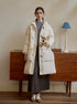 Long white quilted puffer coat with toggle closures over gray sweater and skirt, styled with vintage dresser and blue lamp
