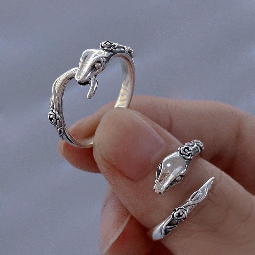 A model is holding a sterling silver snake ring with rose details. The adjustable design features snake head and tail