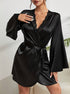 A woman wearing a black silk robe with lace trim neckline, flared sleeves, and waist tie belt, displaying white manicured nails