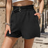 Black textured shorts with double-ring belt detail, paperbag waist and pockets, styled with white crop top against stone wall