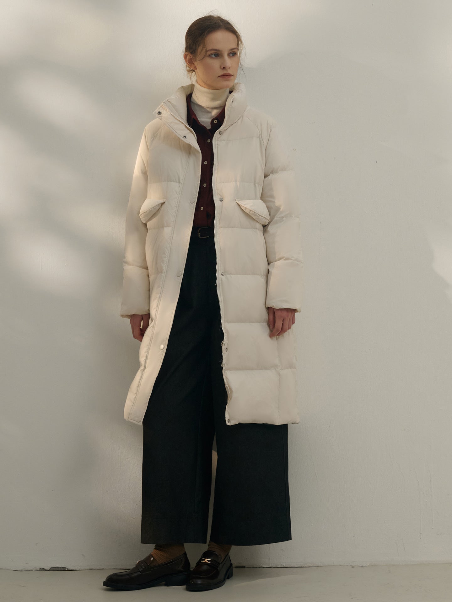 Long white puffer coat with high collar, styled with turtleneck and wide-leg pants, classic minimalist winter look