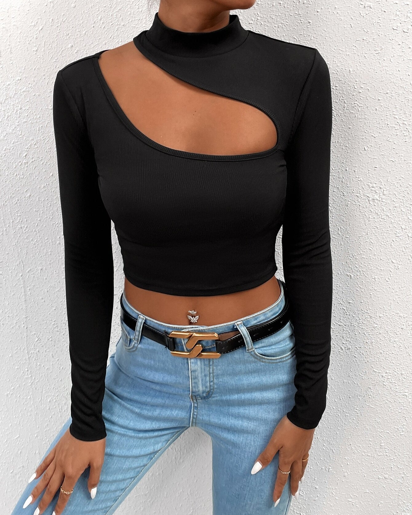 Black long-sleeve crop top with asymmetrical cutout, mock neck, paired with light blue jeans and gold chain belt
