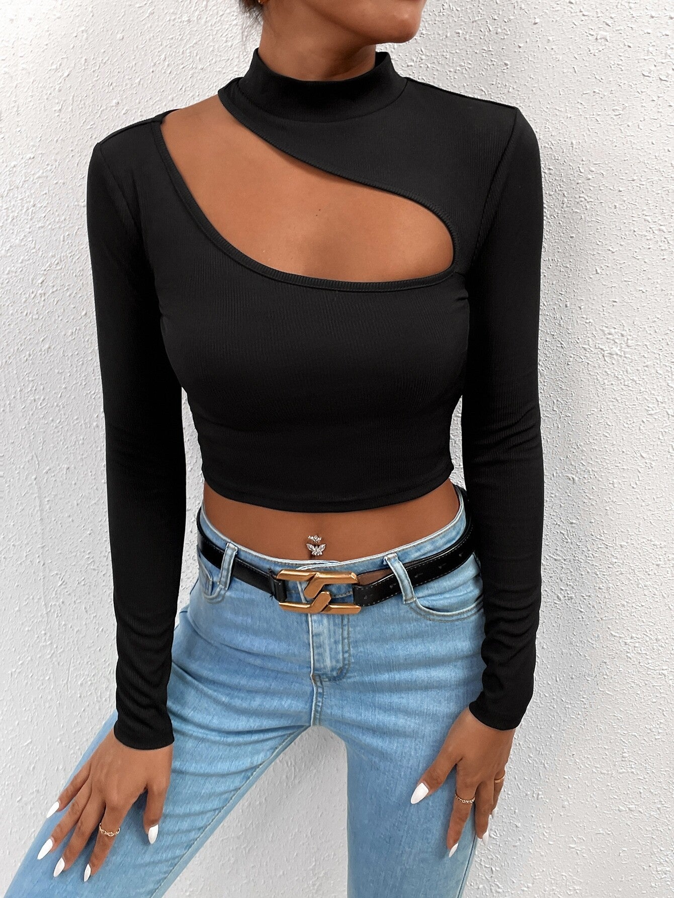 Black long-sleeve crop top with asymmetrical cutout, mock neck, paired with light blue jeans and gold chain belt
