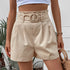 High-waisted beige paper bag shorts with circle buckle belt, styled with white crop top and straw bag