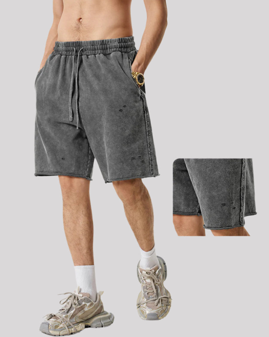 Gray distressed sweatshorts with drawstring waist, shown on model wearing white socks and chunky sneakers