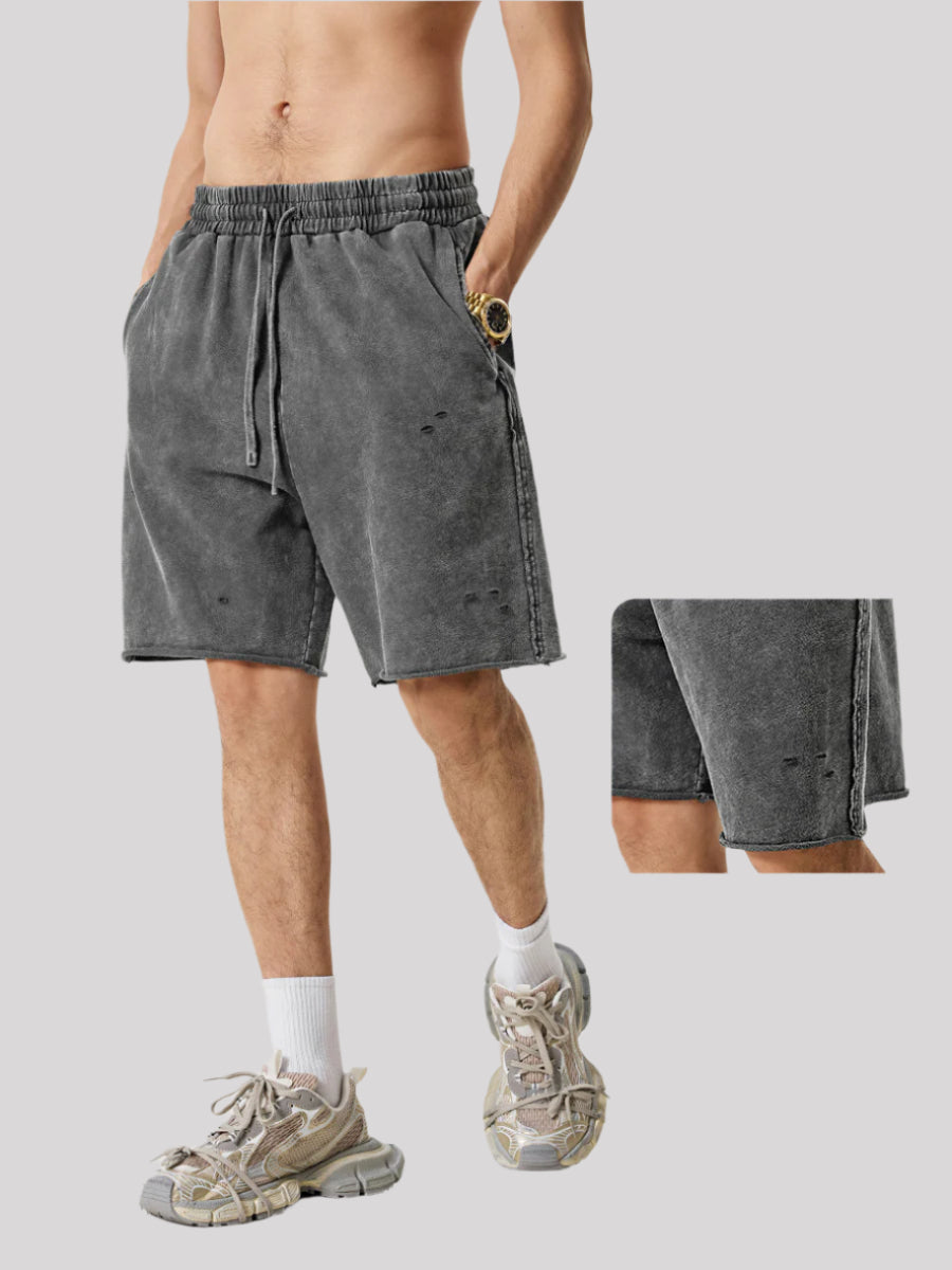 Gray distressed sweatshorts with drawstring waist, shown on model wearing white socks and chunky sneakers