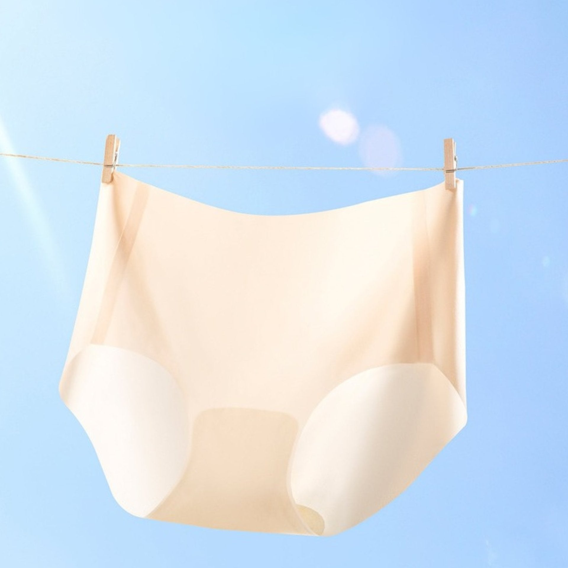 Cream-colored seamless brief hanging on clothesline with wooden clips against blue sky background. 