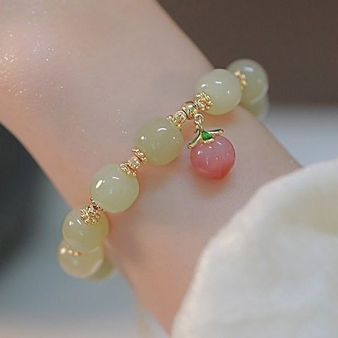 Jade bead bracelet with gold accents and a pink cherry charm, worn on a wrist