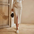 Model wearing cream cargo midi skirt with side slit, white sweater, canvas sneakers, and black chain handbag