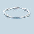 A silver twisted wire bangle bracelet with polished finish displayed against a light blue background