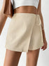Cream textured wrap skort with side tie detail, paired with white crop top and brown leather bag, close-up view of modern design