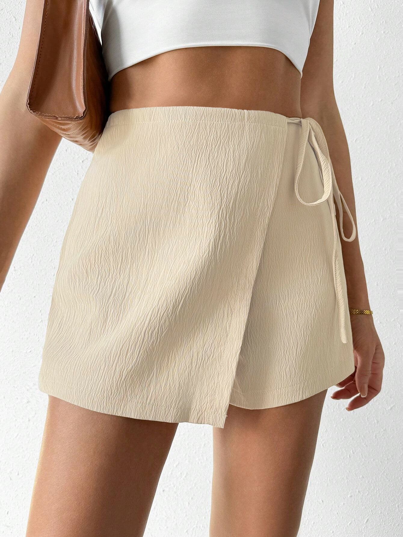 Cream textured wrap skort with side tie detail, paired with white crop top and brown leather bag, close-up view of modern design