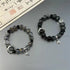 Crystal and black stone bracelet set with silver crescent moon charm, geometric medallions and leaf charm against Chinese calligraphy background