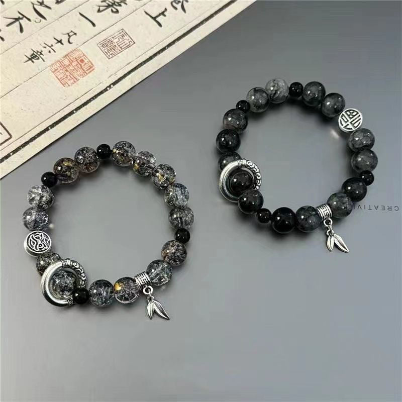 Crystal and black stone bracelet set with silver crescent moon charm, geometric medallions and leaf charm against Chinese calligraphy background