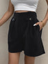 Black high-waisted pleated shorts with button flaps, white crop top, and gold bracelet for chic summer style