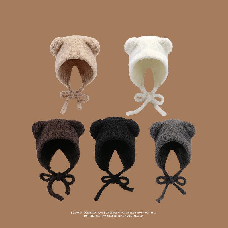 Five plush teddy bear ear hats displayed against a brown background, available in beige, white, dark brown, black, and gray, with tie closures for UV protection