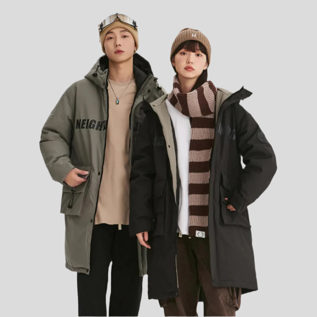A man and woman wearing NEIGHBORHOOD parkas stand together against white background, modeling green and black outerwear with winter accessories