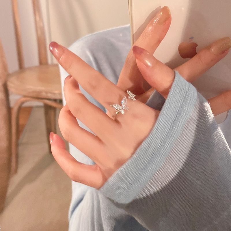 Hand wearing a silver butterfly ring with sparkling stones, holding a phone in a cozy setting