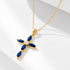 A gold cross pendant with blue sapphire marquise stones and center diamond on delicate chain against white background