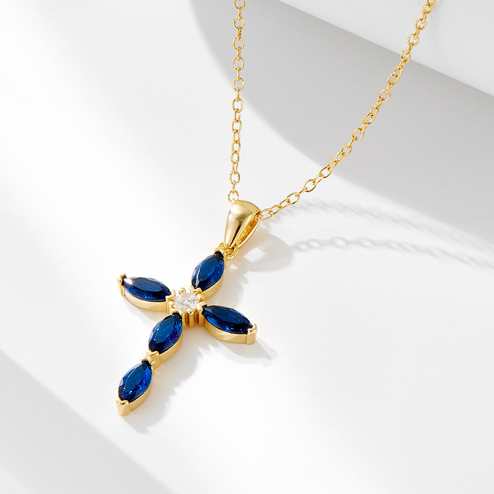 A gold cross pendant with blue sapphire marquise stones and center diamond on delicate chain against white background