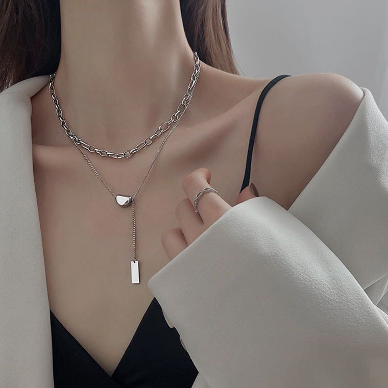 Layered silver chain necklace worn by model, with chunky link chain and lariat-style pendant necklace with small rectangle charm