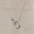 Delicate silver necklace featuring interlocking rings pendant, one with pavé diamonds, on silver chain against neutral background