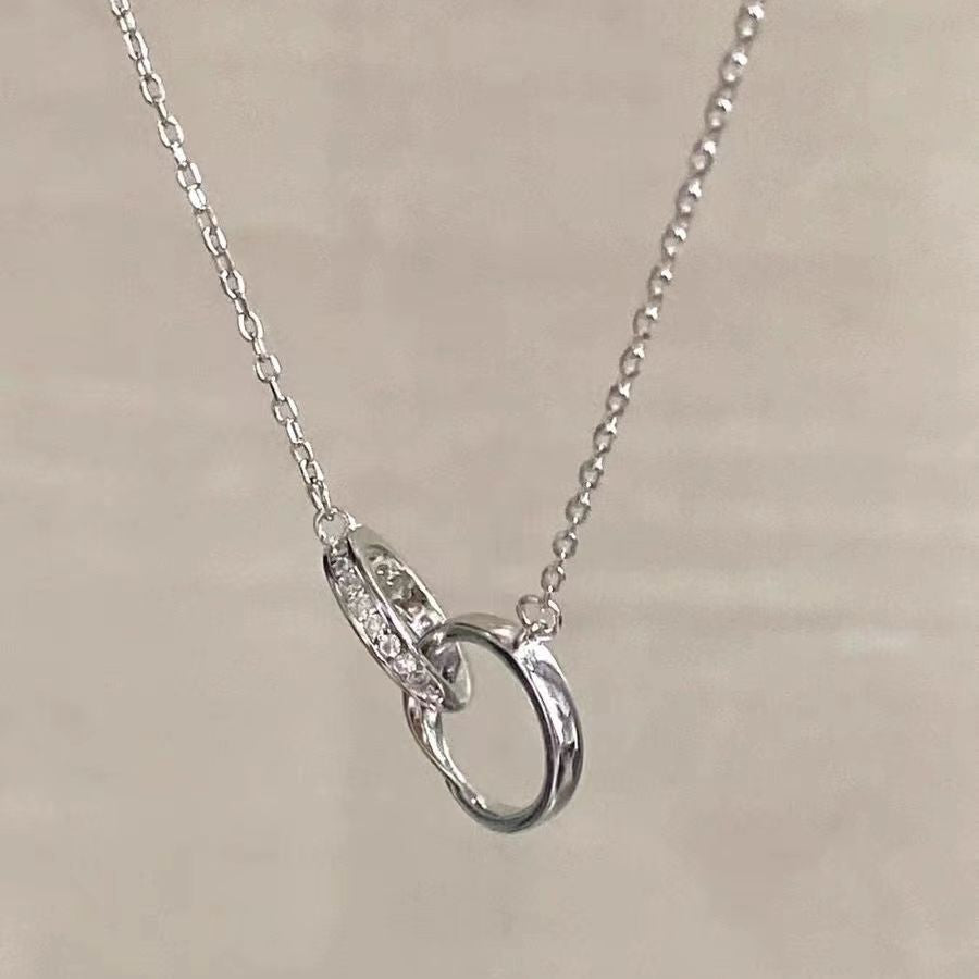 Delicate silver necklace featuring interlocking rings pendant, one with pavé diamonds, on silver chain against neutral background
