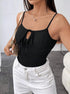 A woman wearing a black ribbed bodysuit with tie-front detail and thin straps paired with white jeans and carrying a beige shoulder bag in a minimalist interior