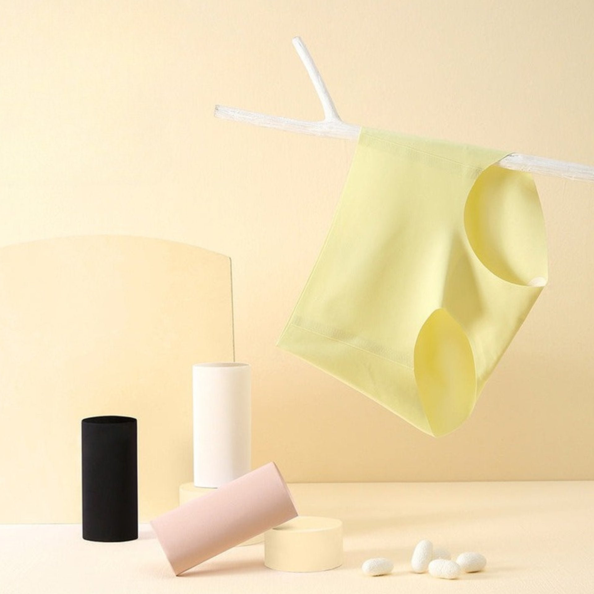 Product display of mulberry silk underwear collection showing yellow brief hanging on string and cylindrical packaging in black, white, and pink.