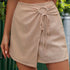 Beige linen-blend mini skort with unique circular ruched tie-front detail, wrap style silhouette against natural backdrop