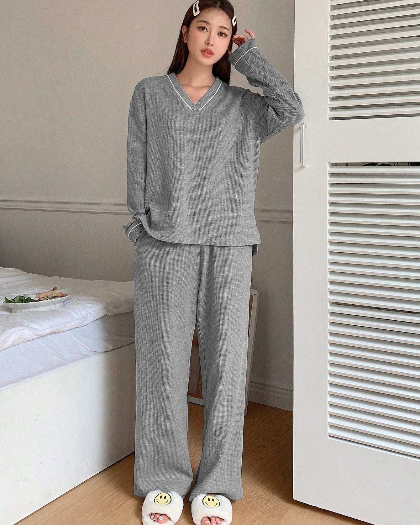 Gray ribbed loungewear set with V-neck top, wide-leg pants, and smiley face slippers in bedroom setting