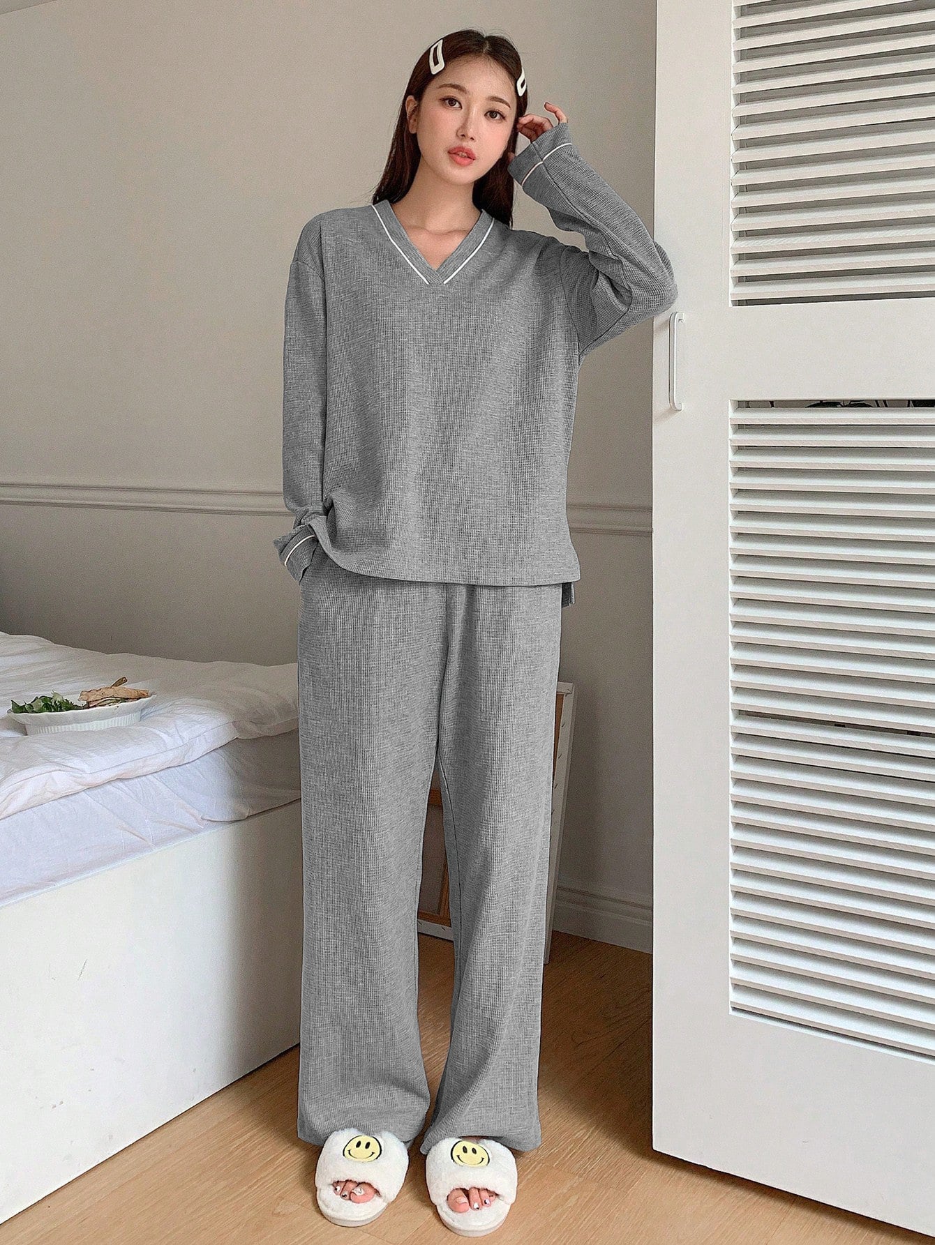 Gray ribbed loungewear set with V-neck top, wide-leg pants, and smiley face slippers in bedroom setting