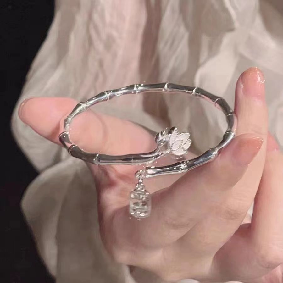 A silver bamboo-style bangle bracelet with lotus flower and charm pendant held in hand against white fabric