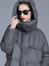 A woman wearing a gray oversized puffer coat with hood pulled up, black sunglasses and red lipstick, touching hood while posing against gray background