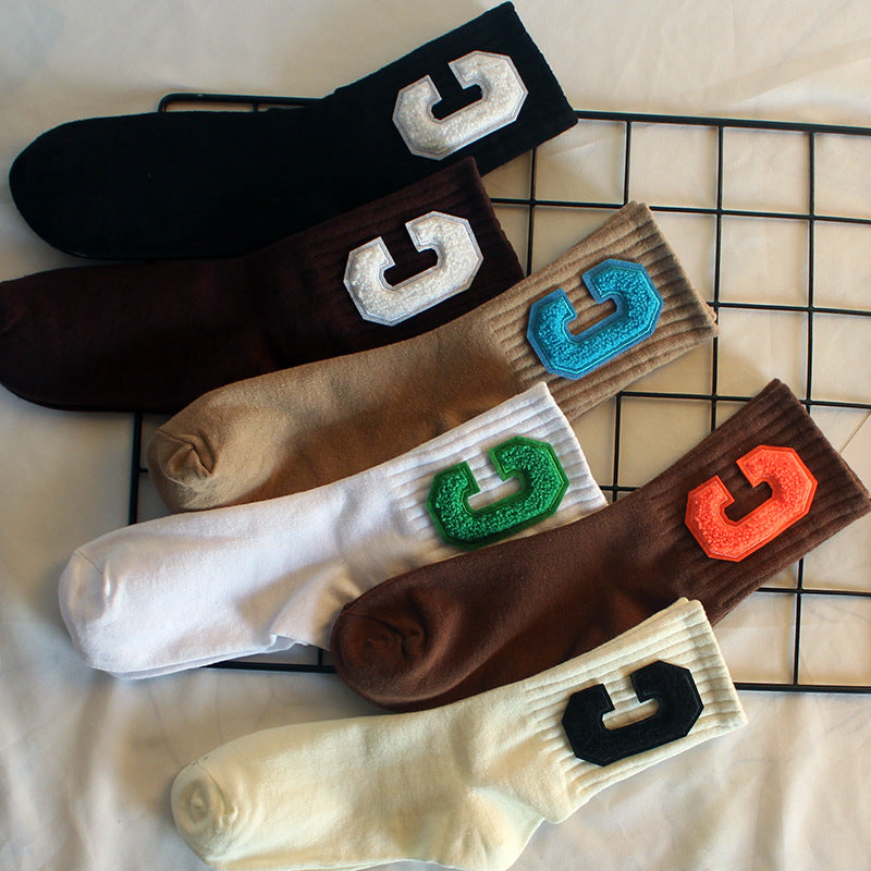 Black, brown, beige, white, and cream crew socks, each featuring a bold varsity-style "C" patch in different colors