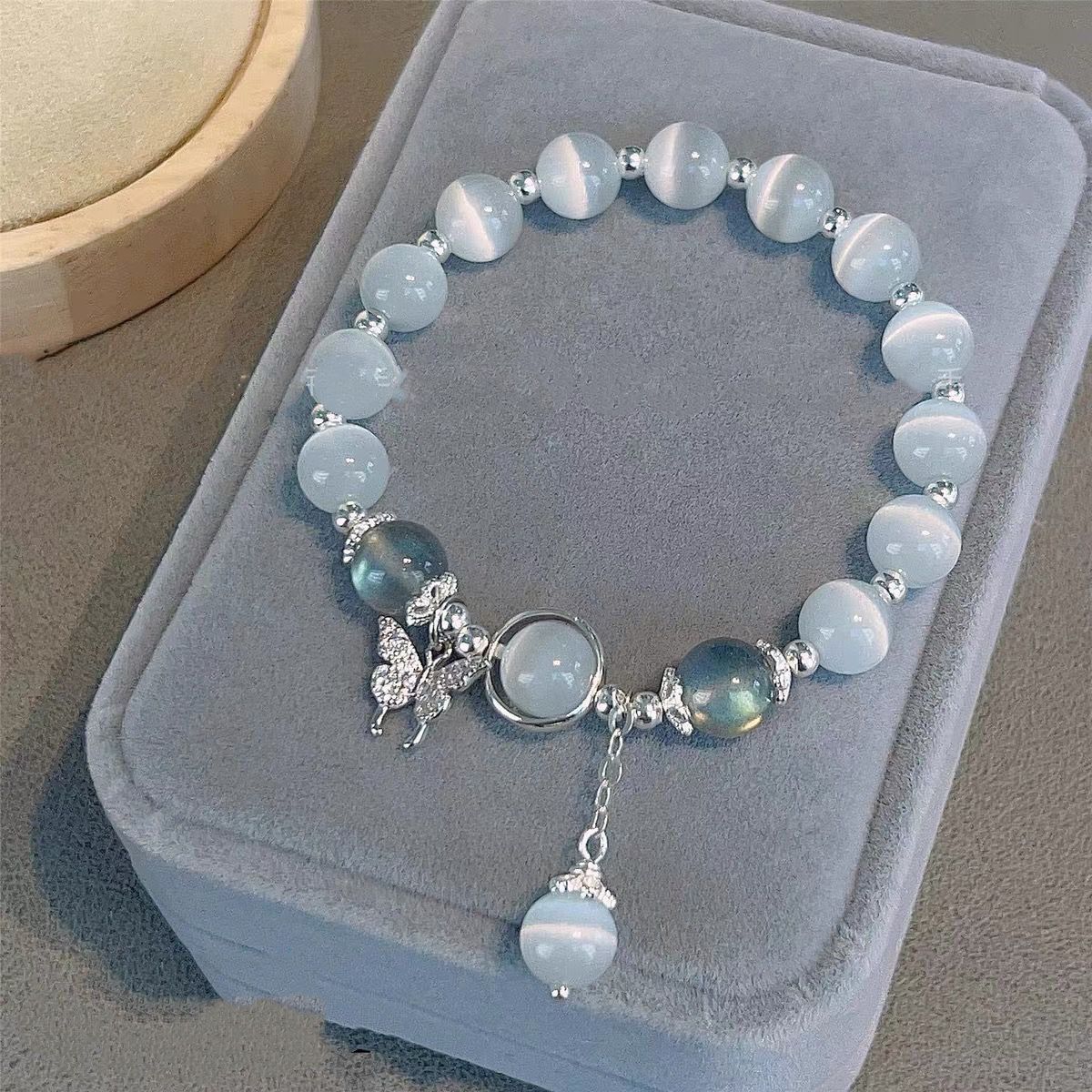 Blue cat's eye crystal bracelet with silver butterfly charm and matching pendant, displayed on grey velvet jewelry box