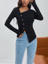 Asymmetric black ribbed top with decorative white buttons, paired with light wash jeans and gold accessories