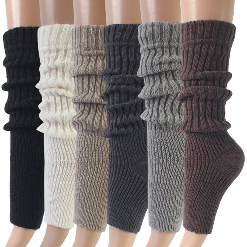 Six pairs of ribbed leg warmers displayed in black, white, gray, and brown tones, arranged in a row on a light background