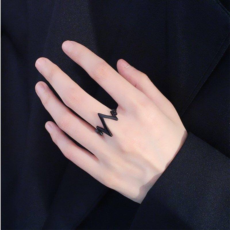 Black lightning bolt ring worn on pale hand against dark fabric background