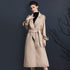 Woman in a beige wool trench coat with a belted waist, wearing a black turtleneck