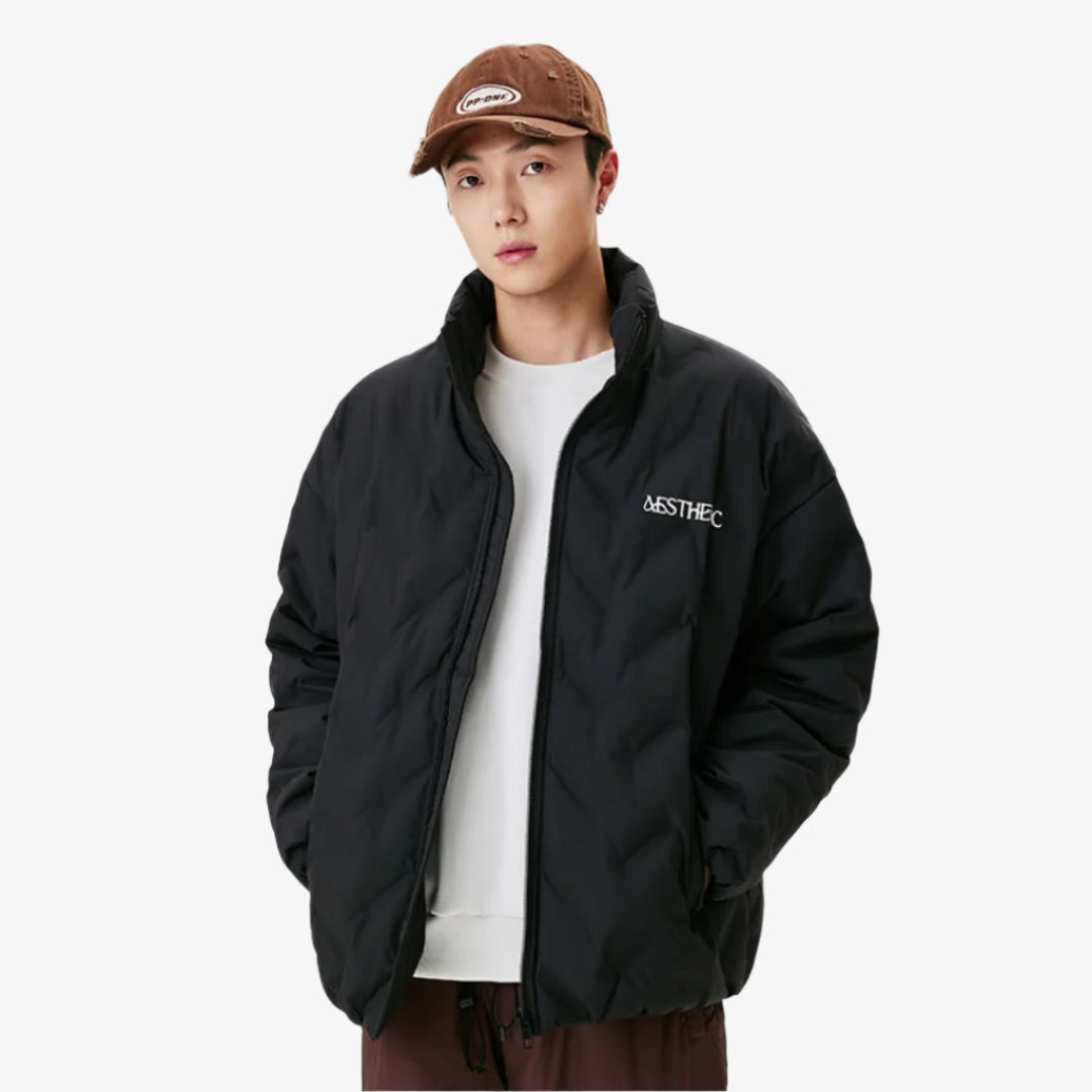 Man wearing black Aesthetic quilted puffer jacket with brown baseball cap and white t-shirt against white background