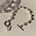 A pearl bracelet with silver links, toggle clasp and butterfly charm displayed on a cream surface next to glass decor