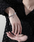 Silver zodiac charm bracelet with layered chains, worn on the wrist with a black textured outfit for an elegant style.