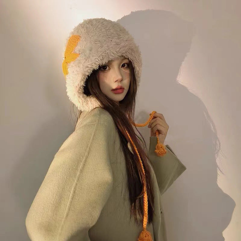 Young woman wearing cream furry winter hat with orange lightning bolt design and matching orange braided ties