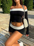 Woman on bench in black/white two-piece with off-shoulder crop top, side ties, shorts and chain-strap handbag