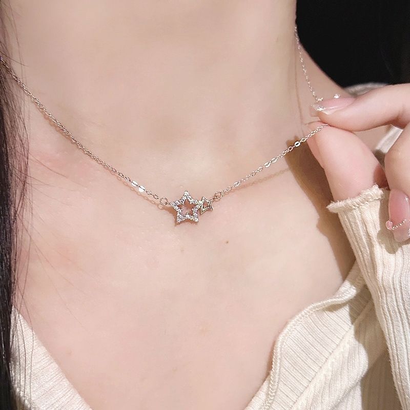 A woman is wearing a dainty silver star necklace with crystal accents against her neck, touching the chain with cream sweater visible